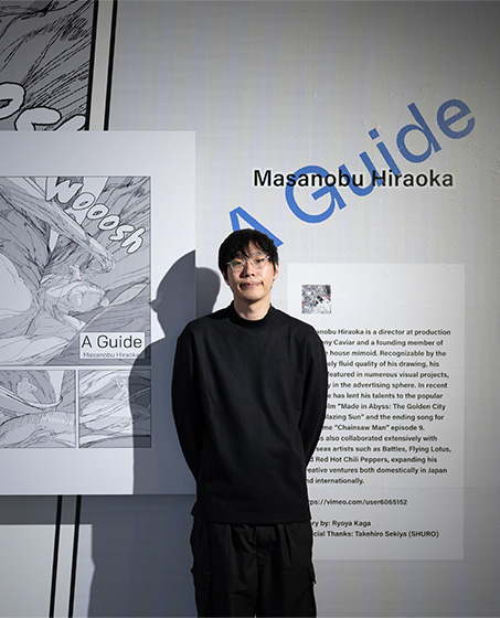 『案内人』の作者・平岡政展が、同作品の展示ゾーンの壁面の前に立っている。