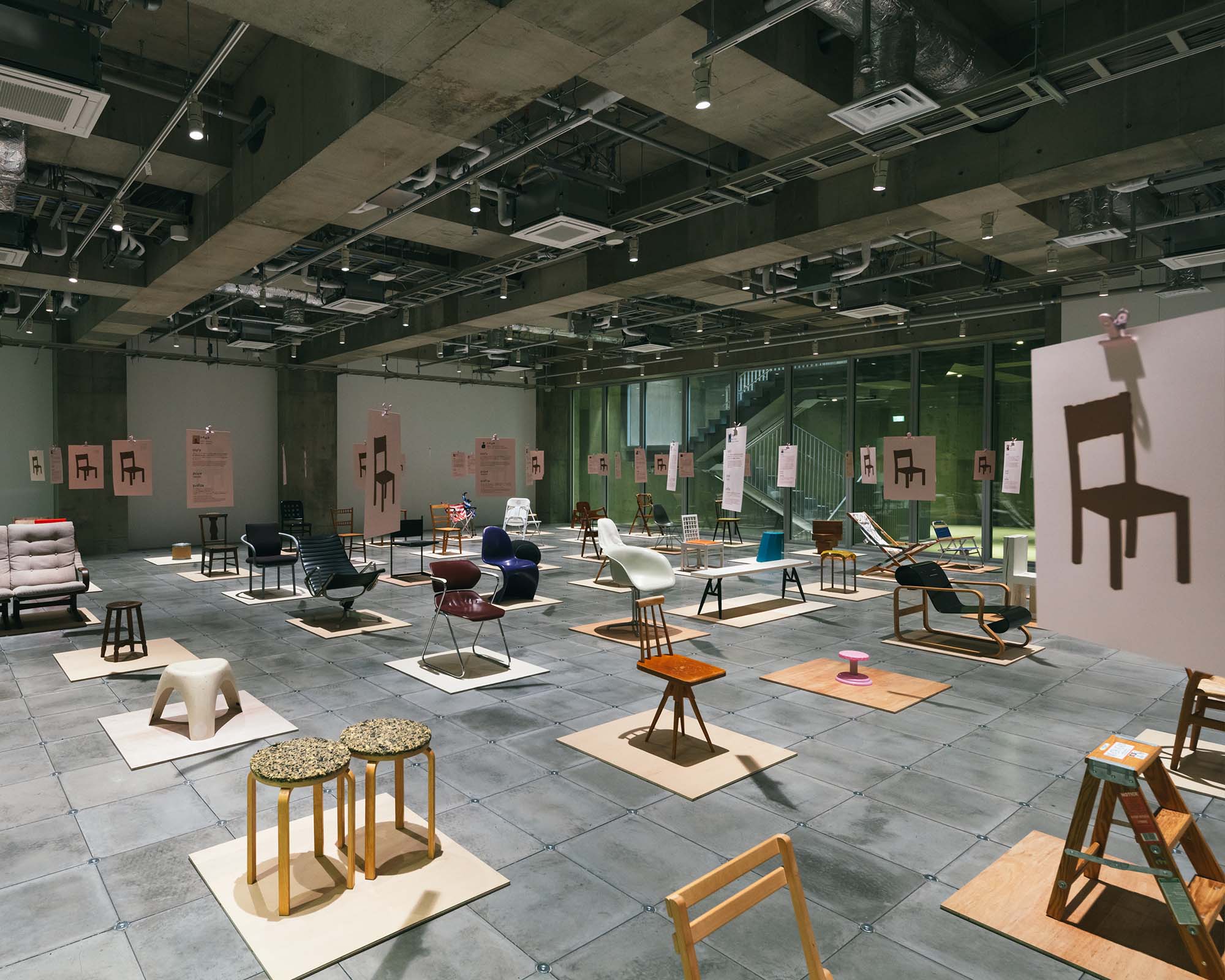 On a wide floor at Ginza Sony Park, distinctive chairs stand on individual platforms, highlighted by concrete architecture and overhead lighting.