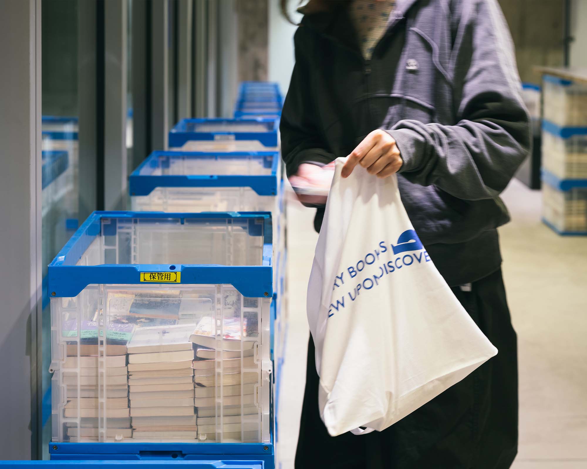 At Ginza Sony Park, a visitor selects a book from a container and places it into a tote bag, capturing a moment of discovery.