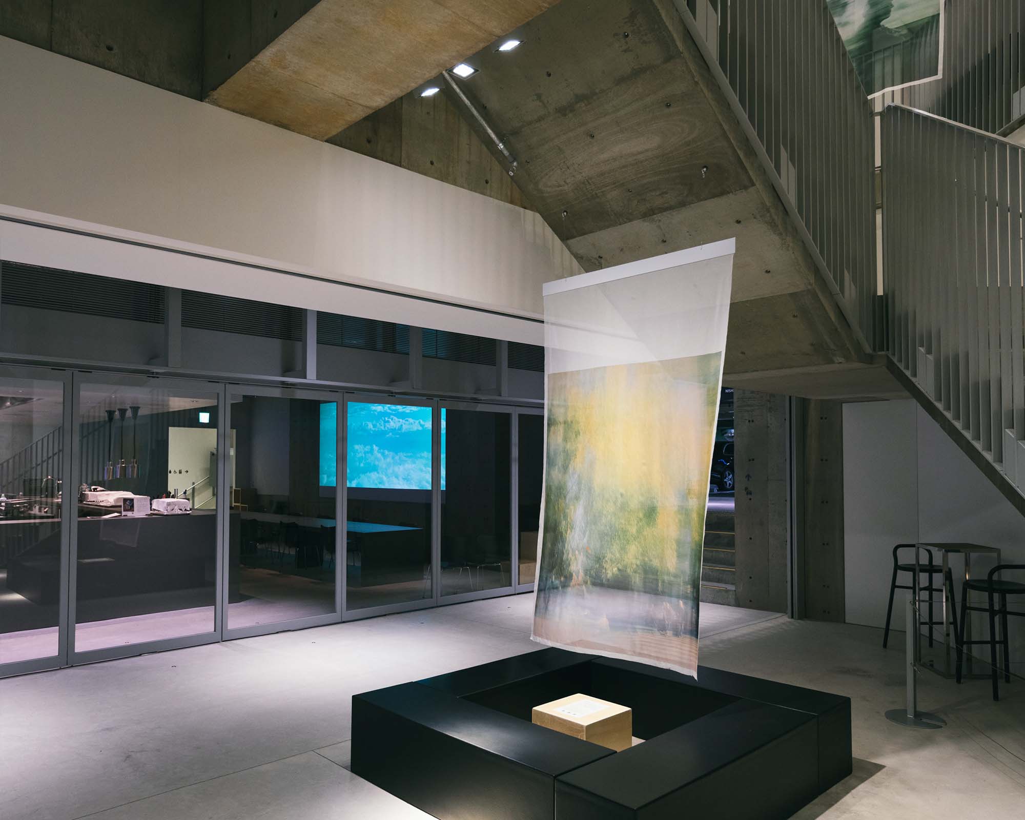 In the atrium of Ginza Sony Park B3, a translucent fabric artwork hangs quietly, framed by concrete beams and stairs, echoing the video projection beyond.