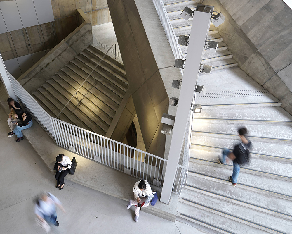 Top-down view of an atrium staircase with people sitting on benches and others moving up and down the stairs.