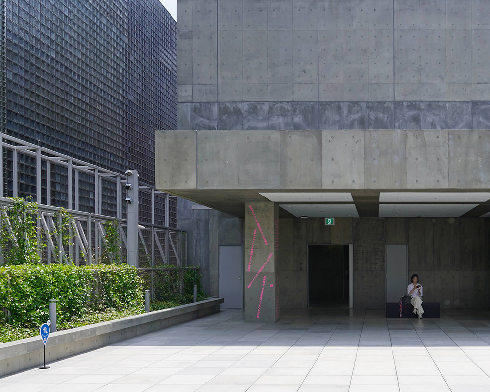 Rooftop terrace of Ginza Sony Park with a visitor seated by a concrete wall, surrounded by greenery in an open space.