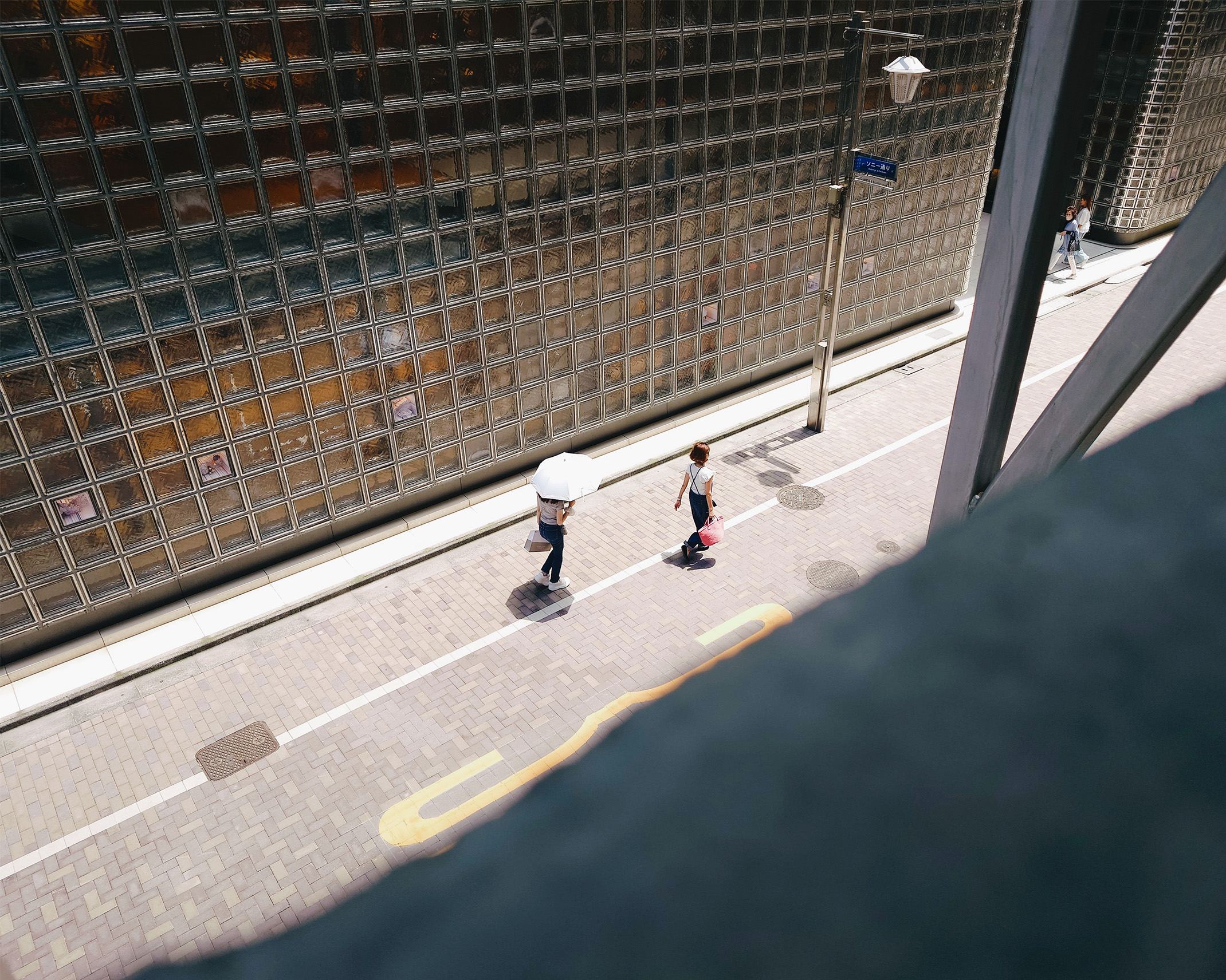A view looking down from within Ginza Sony Park shows people walking with parasols and shopping bags.