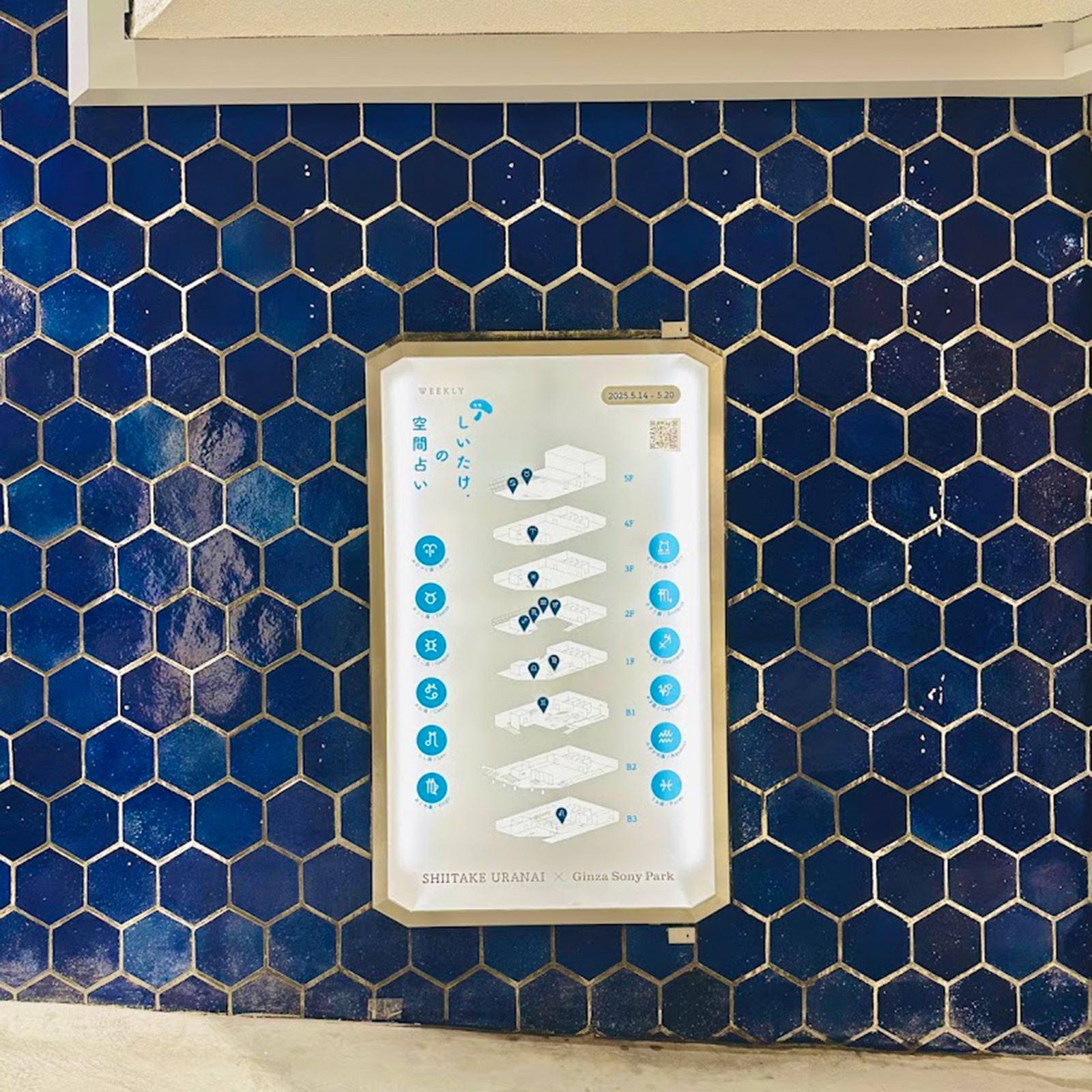 青い六角形タイルの壁に掲示された「しいたけ.の空間占い」の案内パネル。各フロアの位置が示されている。