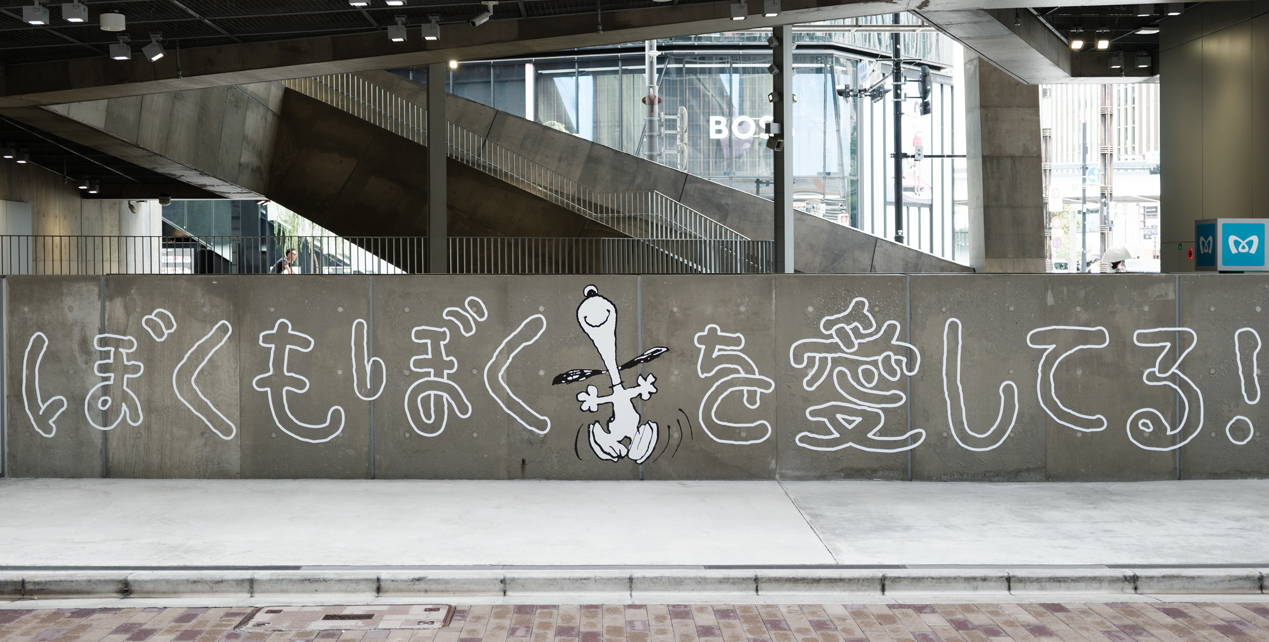 コンクリートの壁に描かれたスヌーピーと白い手書き風の文字「ぼくも ぼくを 愛してる！」。スヌーピーは嬉しそうに両手を広げてジャンプしている。