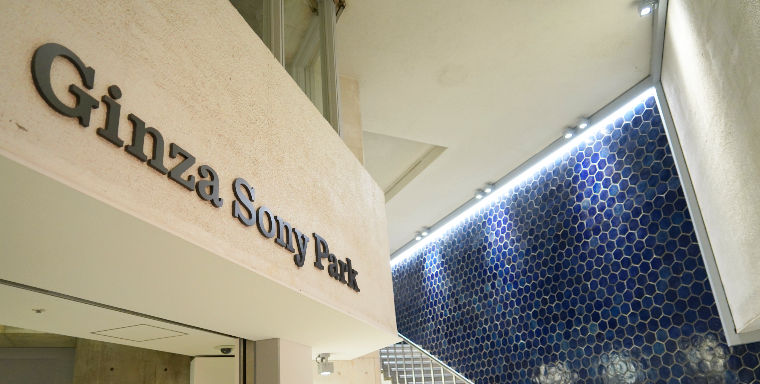 Entrance area of Ginza Sony Park with its logo on the wall, featuring a staircase and a blue hexagonal tiled wall in the background.